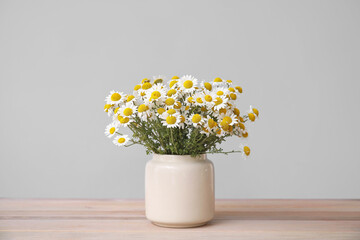Bouquet of fresh chamomile flowers in vase on table against grey background
