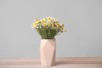 Bouquet of fresh chamomile flowers in vase on table against grey background