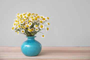 Bouquet of fresh chamomile flowers in vase on table against grey background