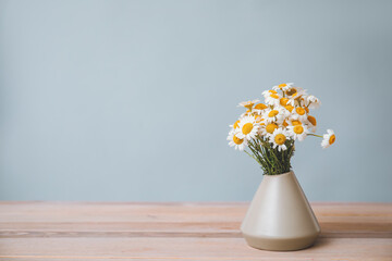 Bouquet of fresh chamomile flowers in vase on table against grey background