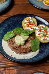 Close up of appetizing and juicy pork patty, grilled with jacket potato and creamy sauce, wooden table of a modern restaurant