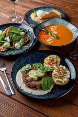 Assorted italian meals on table: pork ground meat patty, cold gazpacho and mozzarella salad, wooden table, dark soft photo