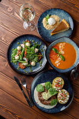 Assorted italian meals on table: pork ground meat patty, cold gazpacho and mozzarella salad, wooden table, dark soft photo
