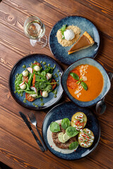 Assorted italian meals on table: pork ground meat patty, cold gazpacho and mozzarella salad, wooden table, dark soft photo