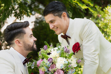 Young married LGBT couples celebrate a romantic wedding ceremony together with a bouquet flower in...