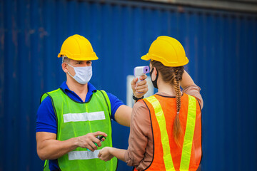 Factory worker man checking fever by digital thermometer for scan and protect from Coronavirus (COVID-19) at cargo containers - Healthcare Concept