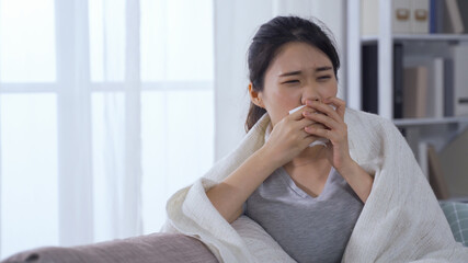 portrait asian female with covid-19 covering mouth with tissue while coughing and rubbing temples...