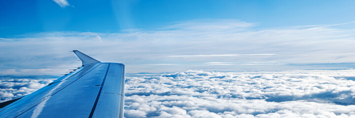 Naklejka premium Airplane wing from window flying above the clouds, aerial view of cloud and sky. Travel concept. Banner.