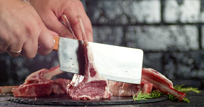 Men's hands with a knife cut raw rack of lamb into pieces. 