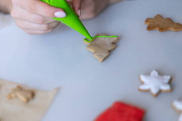 A girl decorates Christmas cookies with green icing sugar.