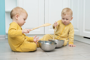 Twin boys play in the kitchen with kitchenware.