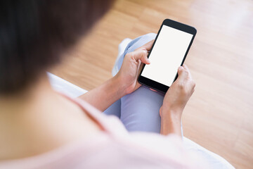Back view close up of a woman hand holding and using smart phone with white blank empty screen sitting on a bed at home