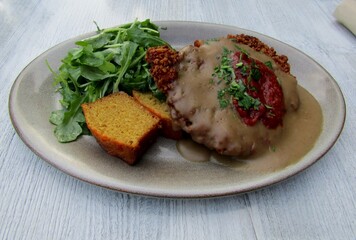Breaded pork schnitzel, corn bread, gravy, and arugula salad on plate.