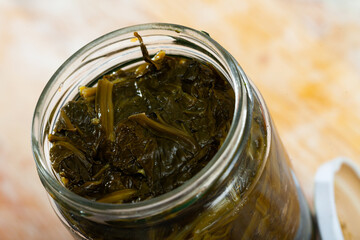 Canned green spinach in opened glass jar on wooden surface, nobody