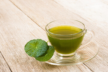 Glass cup of Gotu Kola juice tea with green leaves ( Asiatic pennywort, Indian pennywort, Centella asiatica ) isolated on wood board background.