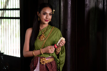 Fototapeta na wymiar Portrait of a beautiful woman in Thai old suit or Thai national dress suit looks elegant and charming in Old antique Thai houses/Old Thai fashion model concept
