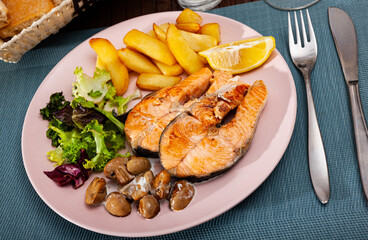Healthy dinner, grilled trout steaks with fresh greens, roasted potato, mushrooms and lemon