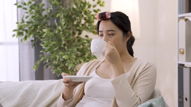 chinese woman with hair curler on her bangs is slacking off sipping hot coffee after a morning shower. indoor and casual style shooting.