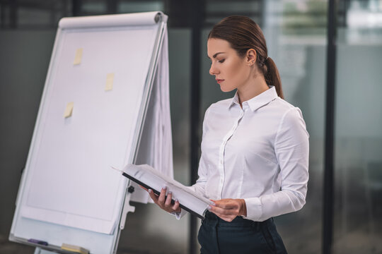 Brown-haired female standing near flipchart, reading papers