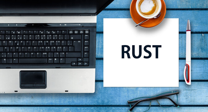 RUST programming language.  Paper width word Rust and laptop, glasses and coffee on wooden table