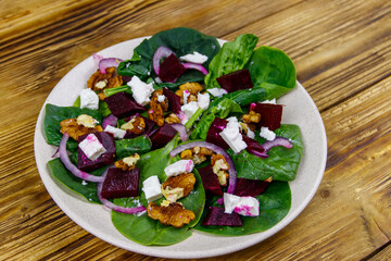 Tasty spinach salad with boiled beetroot, feta cheese, walnut and red onion on wooden table. Healthy vegetarian food