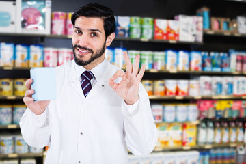 Positive man pharmacist is standing with medicines in pharmacy