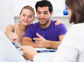 Obraz premium Young smiling couple consulting with female real estate agent in home interior