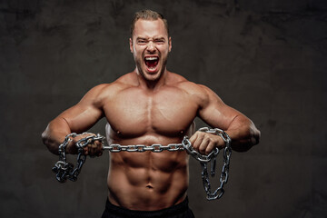 Confident bodybuilder with musculate body and with chains posing and cry in grung background.