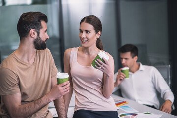 Bearded male and brown-haired female coworkers drinking coffee, talking