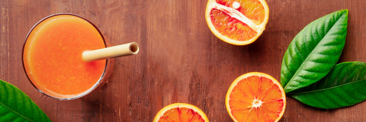 Bamboo straw panorama on a rustic wooden background, fresh orange juice with blood oranges, top shot