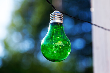 green light bulb hanging in wire outdoors with blurry background
