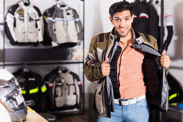Fototapeta na wymiar Smiling man is trying up jacket-equipment for moto in sport store