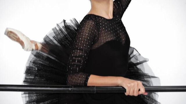 Young ballerina lifting up leg near ballet barre on white background