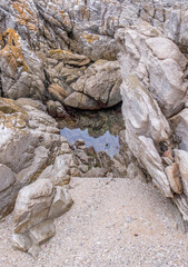 A small rock pond between large rocks with a sandy beach in an isolated spot image in vertical format