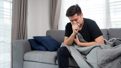 Fototapeta na wymiar Asian man with seasonal infections Cold Blowing His Nose and sneezing into Tissue with headache lying on sofa with high fever and a flu