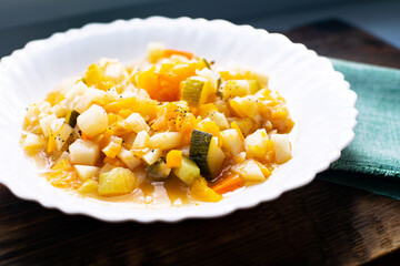 Mix of stewed vegetables on a white plate in cafe. Vegetable stew in tomato sauce. Cooked vegan or vegetarian food.