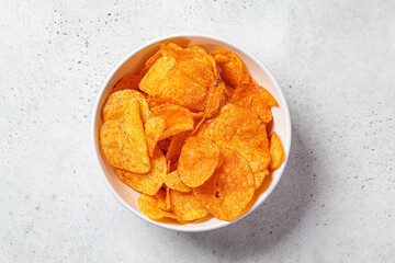 Spicy potato chips in white bowl, gray background, top view. Fast food concept.