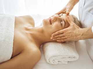 Obraz na płótnie Canvas Beautiful blonde woman enjoying facial massage with closed eyes. Relaxing treatment in medicine and spa center concepts