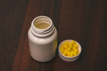 A white medical bottle with a lid and yellow vitamins is isolated on a wooden background. Ascorbic acid. Close-up