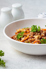 Buckwheat with chicken meat and vegetables in a white plate, white background. Traditional Russian cuisine concept.