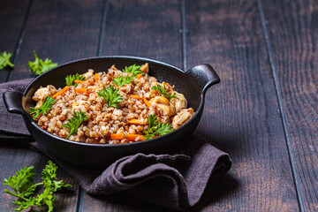 Baked buckwheat with chicken meat and vegetables in black pan, dark background. Traditional Russian cuisine concept.