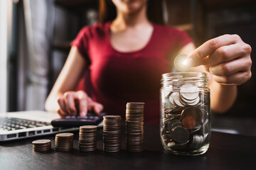 businesswoman holding coins putting in glass with using smartphone and calculator to calculate ...