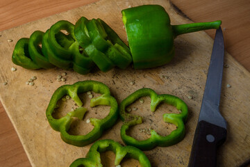 green pepper lies on a cutting board strewn with ground black pepper and seeds along with sliced pepper slices and a knife; cutting green pepper