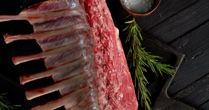 A piece of raw rack of lamb with rosemary slowly rotates. 