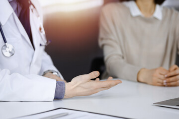 Unknown male doctor and patient woman discussing something while sittingin a darkened clinic, glare of light on the background. Close-up of hands