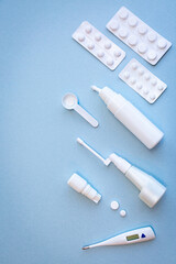 White thermometer, pills, vials with nasal spray and throat spray on blue background