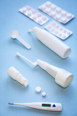 White thermometer, pills, vials with nasal spray and throat spray on blue background