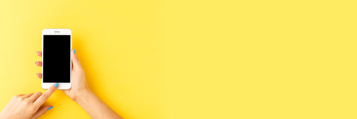 Overhead shot of female hands using smart phone with empty screen on yellow background. Top view