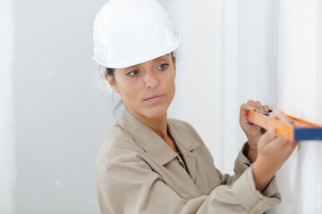portrait of woman holding builders level against wall