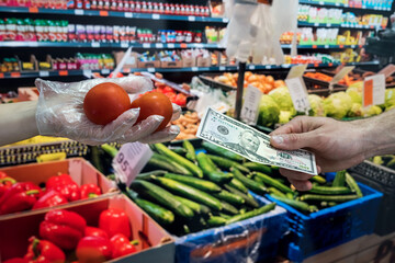 seller in gloves sells fresh vegetables. man gives dollars for groceries in the supermarket.